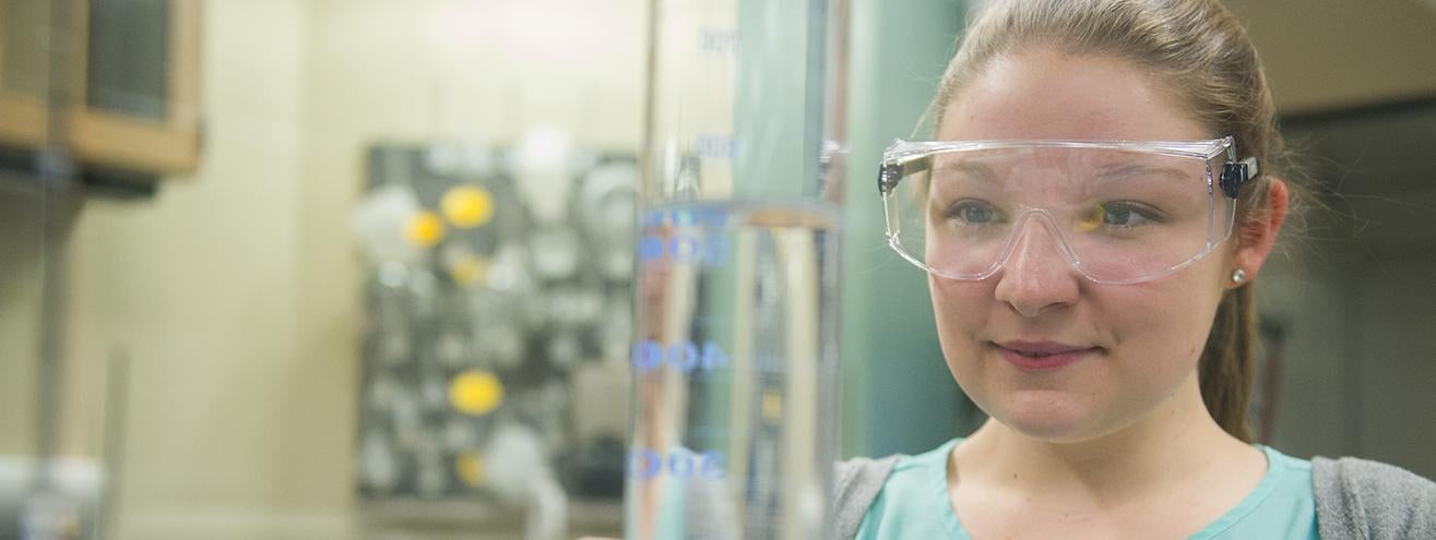 student in safety goggles holding beaker in chemistry lab
