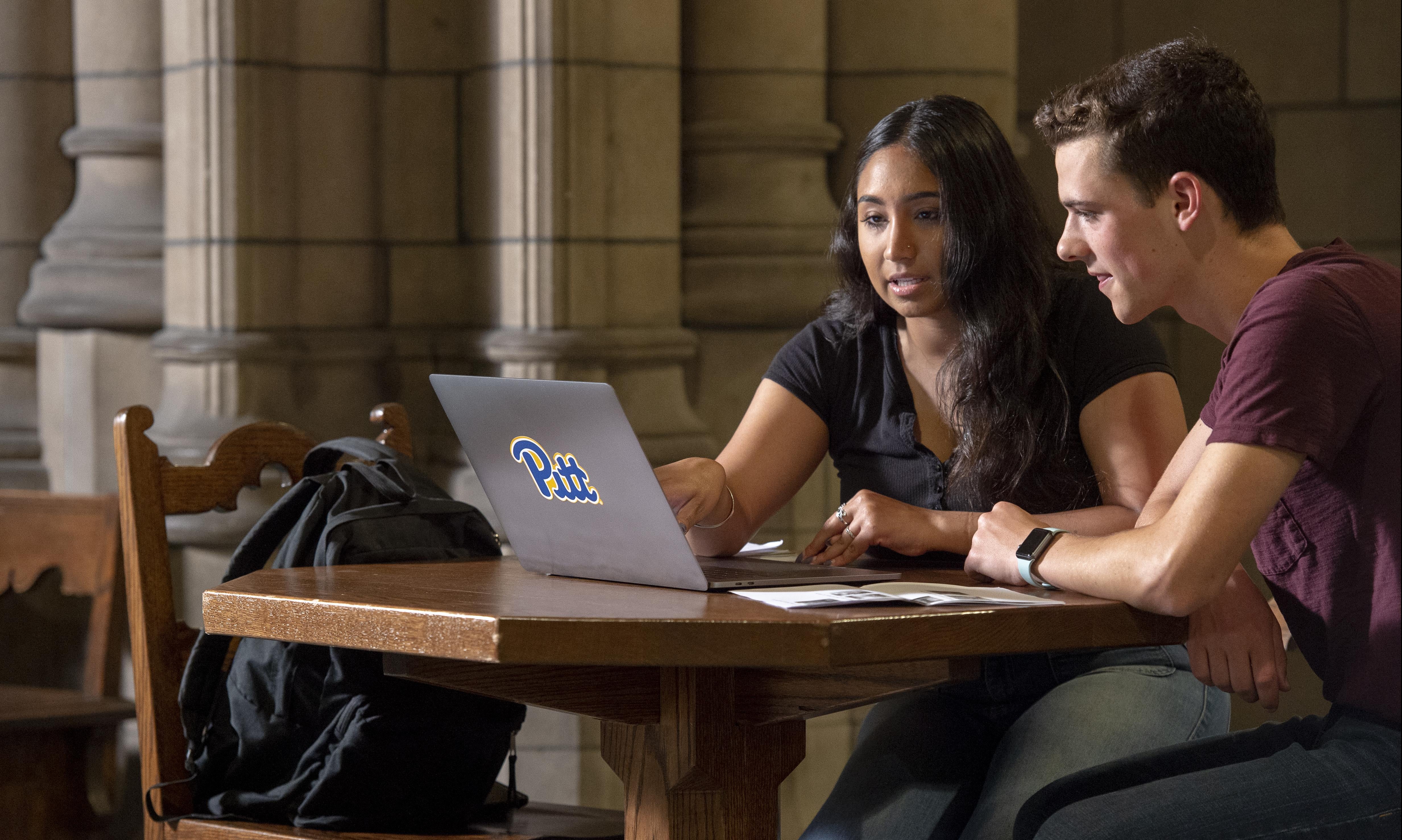 two students studying at table with laptop