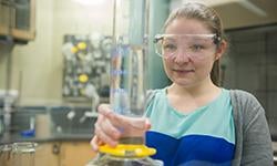 student in safety goggles holding beaker in chemistry lab