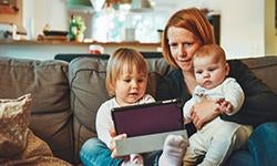mother with infant and toddler on sofa looking at tablet together
