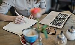 person writing in notebook with laptop